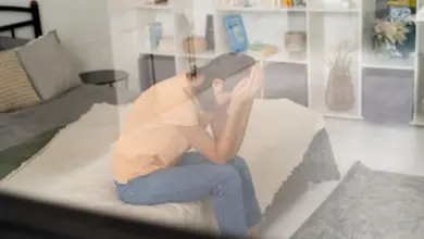 Osoba sedí na posteli s hlavou v rukou při pocitu dezrealizace.