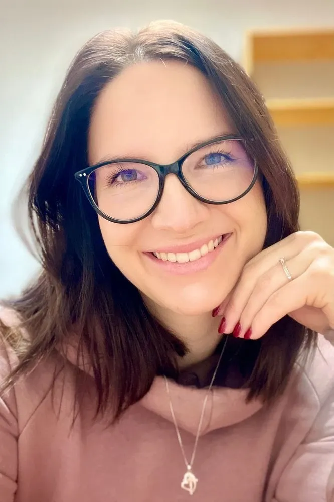 Usměvavá žena s brýlemi se opírá o ruku.