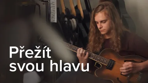 Muž hraje na kytaru v interiéru s textem Přezít svou hlavu.